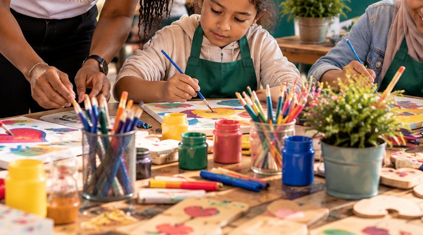A volunteer helping children paint at a community art table.